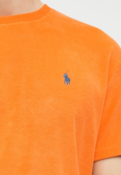Πορτοκαλί μπλούζα από περκάλι με κοντά μανίκια και κεντητό μπλε λογότυπο παίκτη πόλο στο αριστερό στήθος.