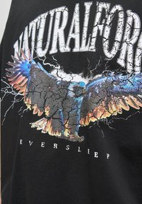 Black t-shirt featuring a graphic design of a colorful eagle with cracked textures, accompanied by the text “NATURALFORCE EVERSLEEP.”
