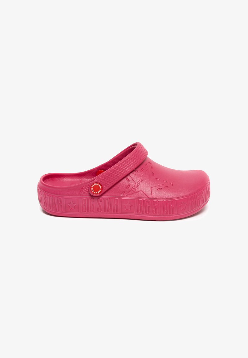 Sabot en caoutchouc rose avec une large sangle et une surface texturée. Présente un marquage proéminent sur le côté et un bouton décoratif rouge.
