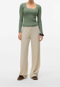 Ljusgrön ribbad långärmad topp med fyrkantig halsringning, kombinerad med beige vida byxor och mörkbruna skor. Mörkt armband som accent.