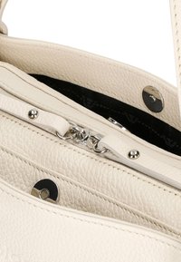 Crème leren handtasinterieur met ritssluiting en zilveren hardware. Heeft een gestructureerd oppervlak en een donkergepatroneerde voering.