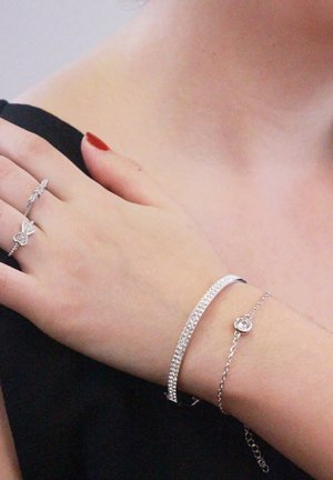 Gioielli d'argento che includono un delicato braccialetto scintillante, un braccialetto a catena sottile con un ciondolo rotondo e un anello decorativo con un design a fiocco.
