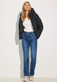 Doudoune noire avec capuche et doublure rose, haut à manches longues blanc, jeans droits bleus et baskets de couleur claire.