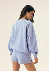 Jasnoniebieski, oversize bluza z długim rękawem, zestawiona z dopasowanymi szortami. Gładka tekstura, luźny krój, brak widocznych wzorów lub akcentów.