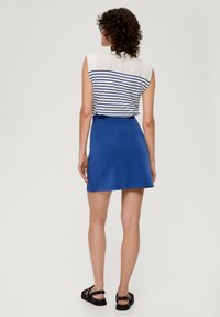 Kurzer blauer Rock, kombiniert mit einem ärmellosen Top in Weiß und Marineblau mit Streifen. Besitzt eine lockere Passform und ein weiches Material. Schwarze Sandalen mit Riemchen.