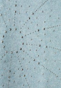 Vaaleansinistä kangasta, jossa on teksturoitu neulospinta, koristeltu metallisilla hopeisilla niiteillä eri kokoisina, järjestettynä säteittäiseen kuvioon.