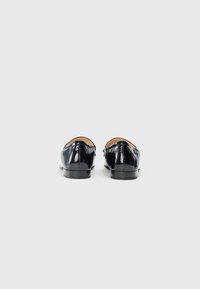 Black patent leather loafers with a smooth, shiny finish, low heel, and decorative stitching detail on the back.