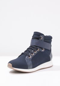 Marinblå hög-top sneakers med en texturerad rem, snörning fram och metalliska accenter. Har en slät ovandel i tyg och gummisula.