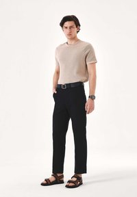 Beežikat tekstuuriga lühikeste varrukatega t-särk, mustad sirge lõikega püksid ja pruunide rihmadega sandaalid. Hõbedane käekell randmel, lihtne must vöö.