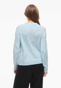 Ljusblå stickad tröja med rund halsringning, långa ärmar och en mjuk textur. Kanten är något längre bak.