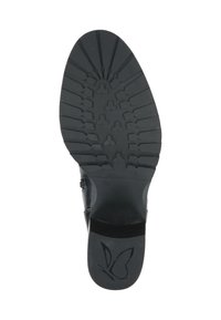 Semelle de chaussure noire avec une surface en caoutchouc texturé, présentant un motif de semelle et un logo en relief en forme de papillon sur la zone du talon.