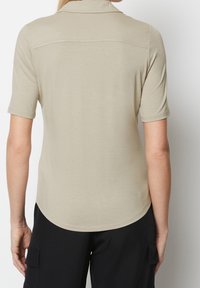 Beige kortærmet polo shirt med krave, glat tekstur, buet sømkant og kontrastfarvede syninger ved skuldrene.