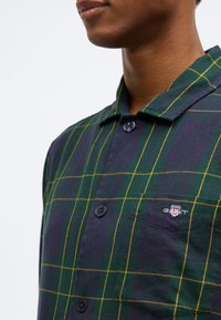 Camicia a maniche corte a quadri in verde scuro e blu navy con righe gialle, con colletto, chiusura a bottone e un piccolo logo ricamato sul petto.