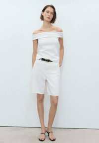 Witte off-shoulder top, witte shorts, zwarte riem met ronde gesp en zwarte platte sandalen. Glad textuur, casual ontwerp, minimalistische stijl.