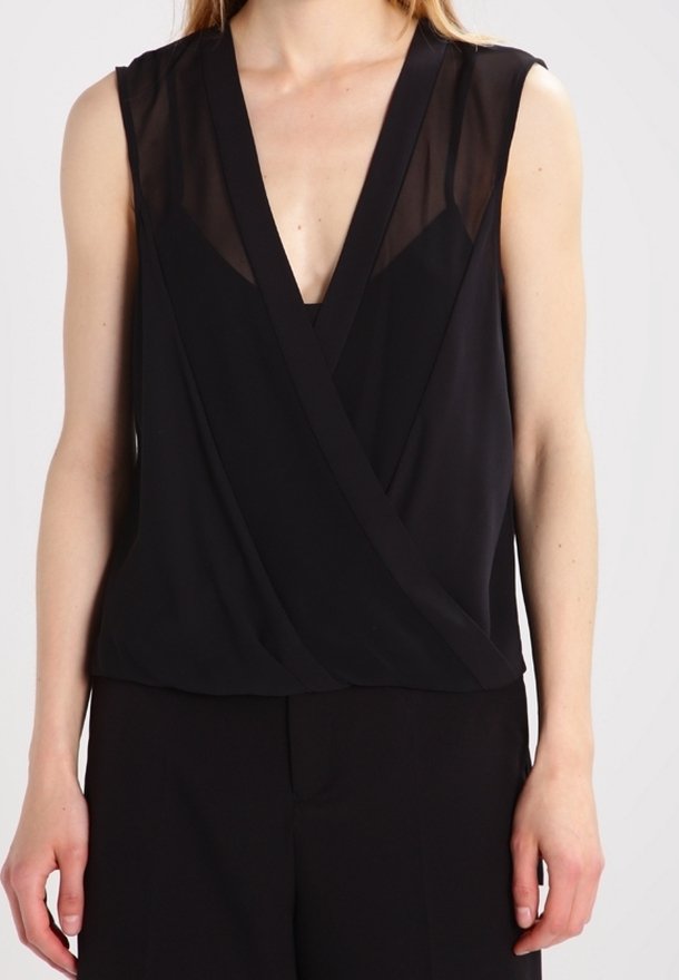 Blouse noire sans manches avec un panneau supérieur transparent et un profond décolleté en V portée par une personne debout, les bras détendus le long du corps.