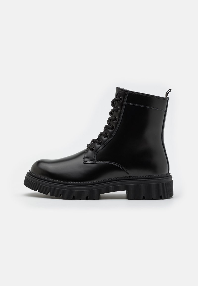 Melna ādas potīšu zābaks ar apaļu purngalu, saistēm, struktūru uz apakšas un cilpu aizmugurē, lai vieglāk uzvilktu.