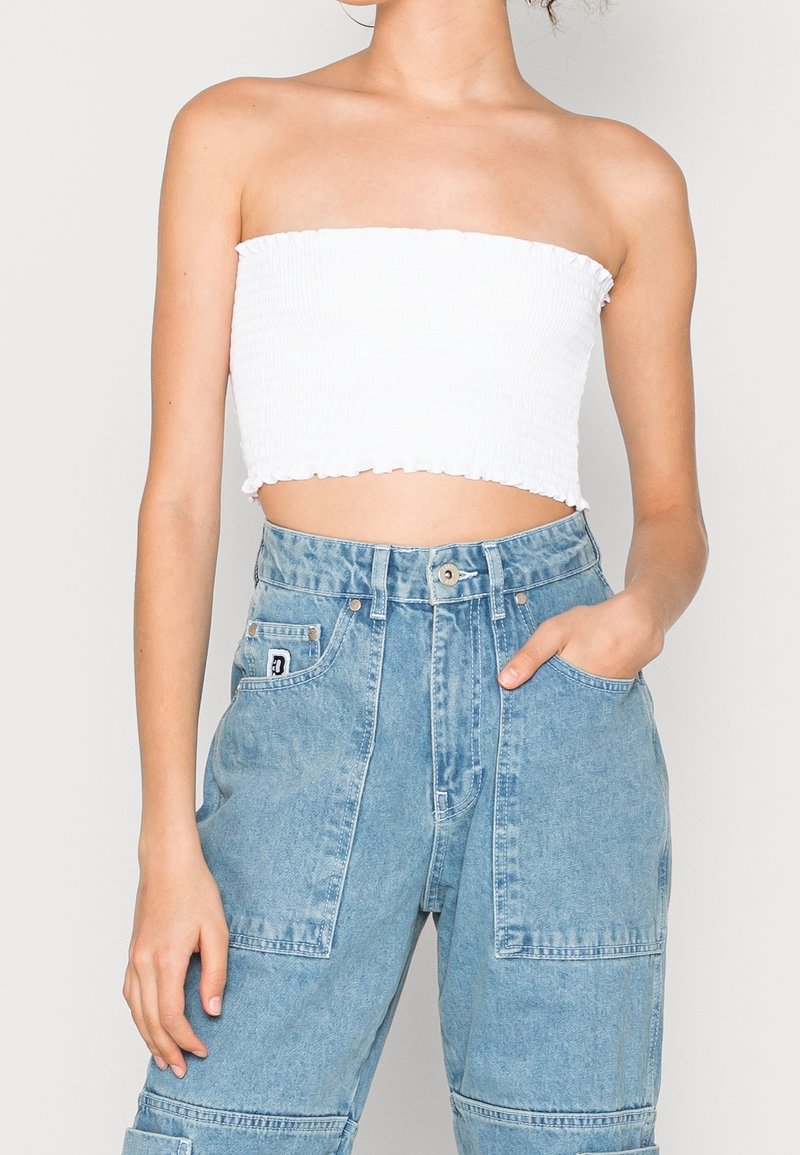 Haut court blanc sans bretelles en coton côtelé avec bords volantés, associé à un pantalon cargo en denim bleu clair taille haute, avec poches plaquées et fermeture à boutons.