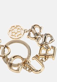 Bracciale in tono oro con ciondoli a lettere intrecciate, accenti di strass trasparenti e un pendente rotondo con logo che presenta motivi intagliati intricati.