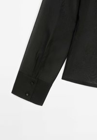 Musta läpikuultava pitkähihaista paitaa napillisilla manseteilla. Sujuva pinta ja räätälöity malli, jossa on kaksi mustaa nappia mansetissa.