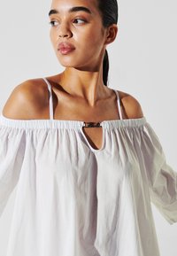 Witte off-the-shoulder blouse gemaakt van lichtgewicht stof, met een gathered halslijn, een keyhole-cutout en een metalen accent aan de voorkant.