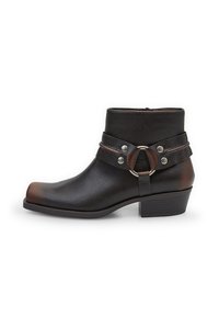 Bota de tobillo de cuero negra con punta redondeada, detalles de hardware plateado y una correa con un hebilla circular. Diseño de tacón bloque.