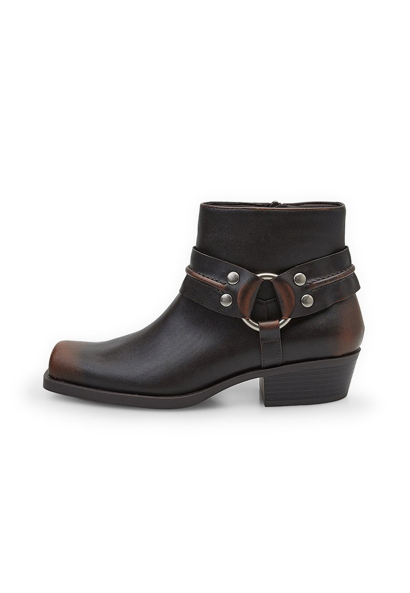 Bota de tobillo de cuero negra con punta redondeada, detalles de hardware plateado y una correa con un hebilla circular. Diseño de tacón bloque.
