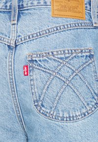 Vaaleansiniset farkut sisältävät takataskun, joka on varustettu erottuvalla ristikkäisellä ompelukuvioilla sekä punaisella Levi's-logo-tunnuksella.