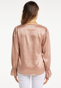 Blusa color oro rosa con un motivo goffrato sottile, maniche lunghe con polsini arricciati e una texture morbida e lucida.