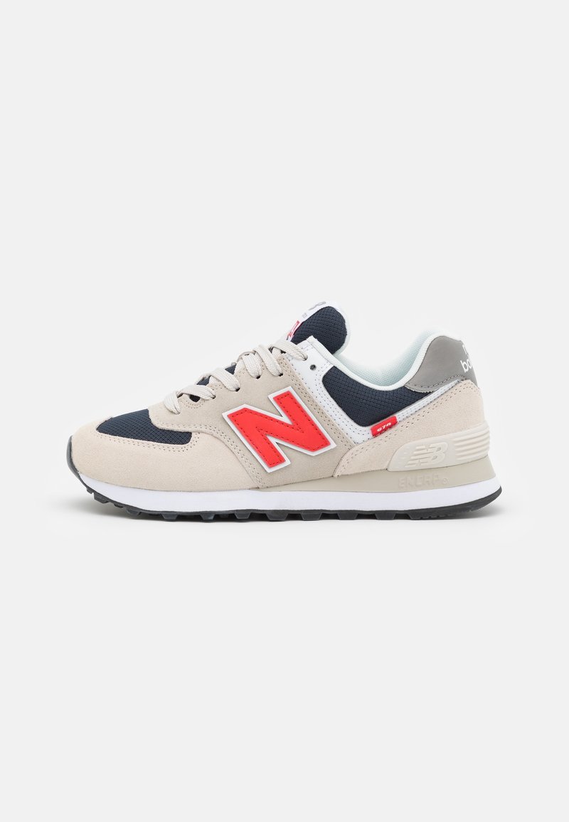 Beige und marineblaue Sportschuhe mit einem roten Logo, aus Mesh- und Wildledermaterialien, gepolstertem Kragen sowie einer kontrastierenden weißen Zwischensohle und schwarzen Laufsohle.