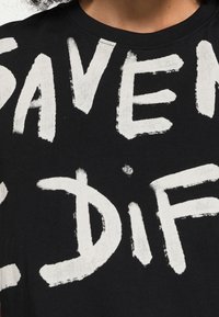 Czarna bawełniana koszulka z dużym białym napisem przypominającym pociągnięcie pędzla: „SAVEN DIFF.” Okrągły dekolt i miękka tekstura. Brak dodatkowych wzorów.