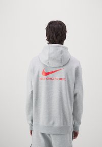 Szara bluza z kapturem, z dużym czerwonym logo Nike oraz napisem "NIKE ATHLETIC DEPT." na plecach. Wykonana z miękkiej tkaniny.