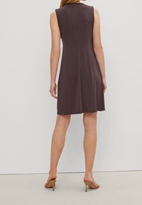 Ärmelloses, knielanges Kleid aus dunkelbraunem Stoff mit glatter Textur und schlichtem Design. Tragen mit hellbraunen, hohen Sandalen.