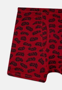 Boxer shorts rouges arborant un motif en répétition du logo "STAR WARS" en noir. Fabriqués en tissu doux avec une taille élastique confortable.