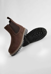 Bottines Chelsea en cuir marron avec des panneaux élastiques sur les côtés et une semelle en caoutchouc noir robuste, présentant une texture antidérapante et de subtils détails de couture.