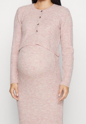 Femme enceinte portant une robe de maternité rose en maille côtelée avec des manches longues et quatre boutons sur la poitrine.