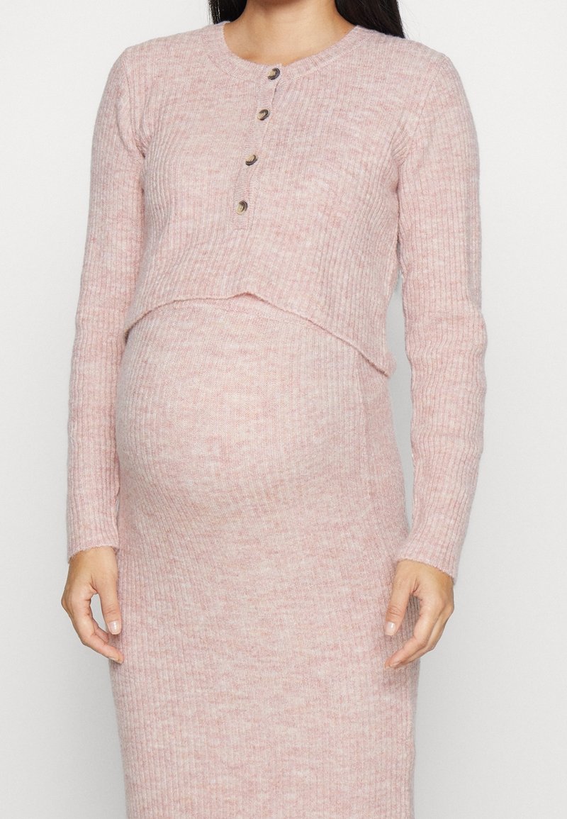 Femme enceinte portant une robe de maternité rose en maille côtelée avec des manches longues et quatre boutons sur la poitrine.