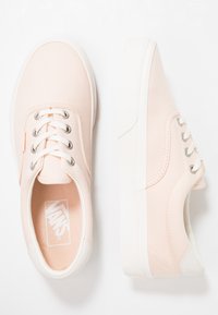 Tenisky Vans s horní částí z lehkého růžového plátna, bílou gumovou podrážkou a stříbrnými očky. Na stélce je logo a texturované akcenty.
