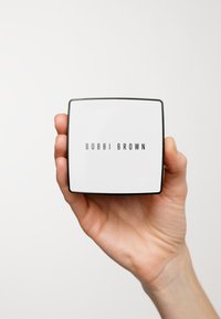 Quadratischer kompaktes Spiegel mit einer glänzenden weißen Oberfläche und schwarzen Rändern. Der Markenname "BOBBI BROWN" ist zentriert in fetten schwarzen Buchstaben.
