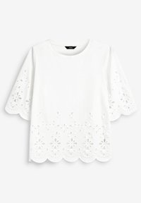 T-shirt en coton blanc à manches courtes, avec des bords festonnés et des détails découpés floraux en bas et sur les manches.