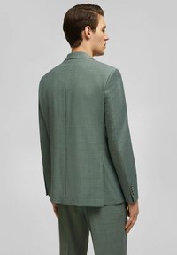 Donkergroene op maat gemaakte blazer, gestructureerde stof, enkele split, geknipte revers, drieknoopsoor, aansluitende snit, bijpassende broek.