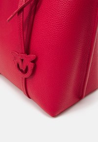 Coin de sac en cuir rouge texturé avec un détail en cuir cousu en forme de papillon, fixé à une fine sangle.