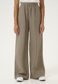 Wide-leg pants in a beige, ribbed fabric with an elastic waistband, featuring vertical stripes. Worn with white shoes.