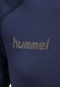 Marine atletikbeklædning med en glat tekstur, hvor ordet "hummel" i lys grå er præsenteret hen over brystet. Syningerne er synlige.