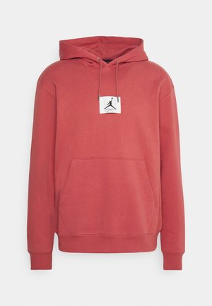 Sweat à capuche rouge à enfiler avec poche avant, cordons et petite étiquette blanche avec logo Jumpman noir et signature sur la poitrine.