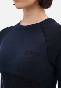 Dunkelblauses Sportshirt mit rundem Ausschnitt, Raglanärmeln und strukturiertem Stoff. Verfügt über ein dezentes Logo in der Nähe des Kragens.