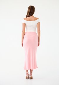 Top bianco scollato con spalle scoperte abbinato a una gonna maxi aderente di un rosa pastello. L'outfit ha una consistenza liscia e un design minimalista.