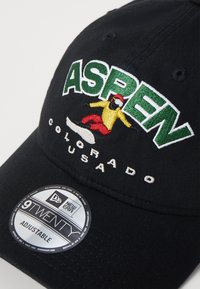 Gorra negra con correa ajustable, con bordado en verde y blanco de "ASPEN" y una figura colorida de snowboard. Logo New Era 9TWENTY en la parte inferior.