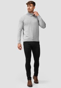 Pull en col roulé gris en tricot doux, coupe près du corps, associé à un jean skinny noir et des bottines marron.