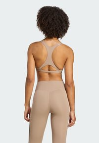 Sujeción deportiva beige con un diseño de espalda de nadador, que presenta un detalle recortado. Combinada con unos leggings de cintura alta a juego, de textura suave y corte ceñido.