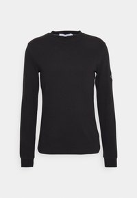 Black long-sleeve cotton shirt with ribbed texture, crew neck, and fitted cuffs. Features a small logo on the left sleeve.